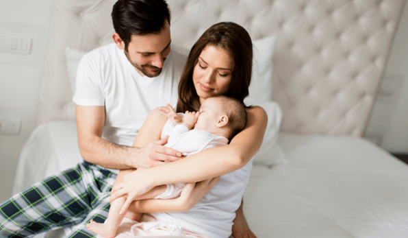 young couple in their pajamas holding small infant in bed
